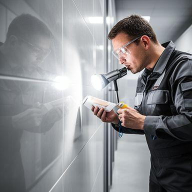 Quality inspector checking reflective ceramic tile under bright light in a clean hallway